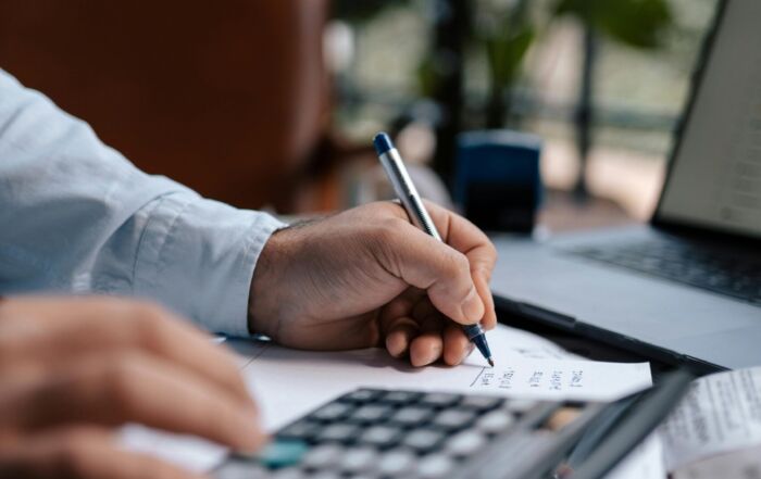 Free A person calculating finances with a calculator and pen on a desk indoors. Stock Photo