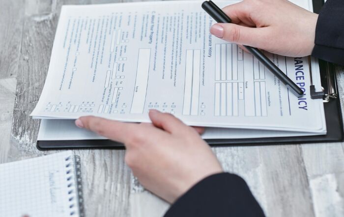 Free Close-up of hands analyzing insurance policy paperwork with pen on table. Stock Photo